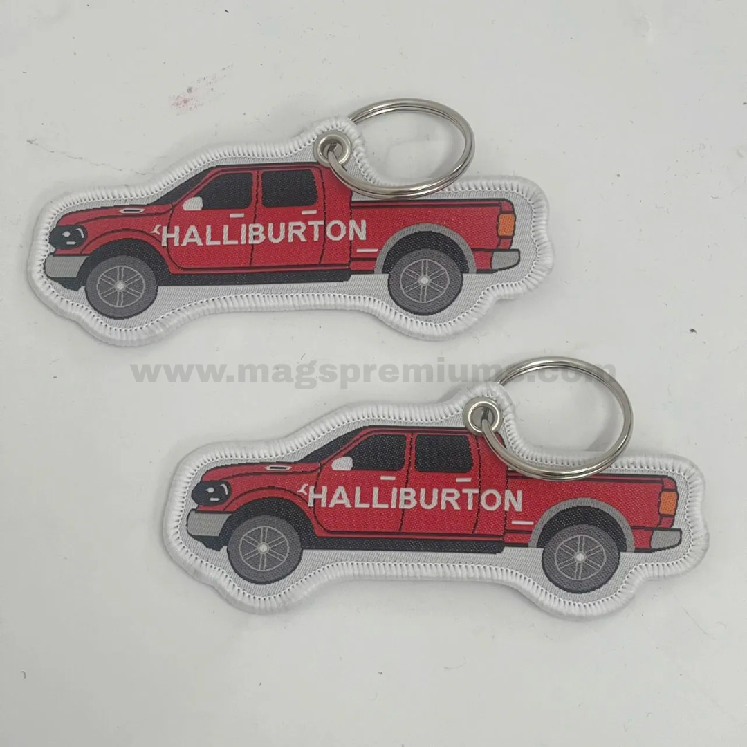 Woven Keychain Custom woven keychain in the shape of a red pickup truck with Halliburton logo, featuring embroidered edge stitching, full-colour woven design, and metal key ring attachment for promotional giveaways and corporate branding.